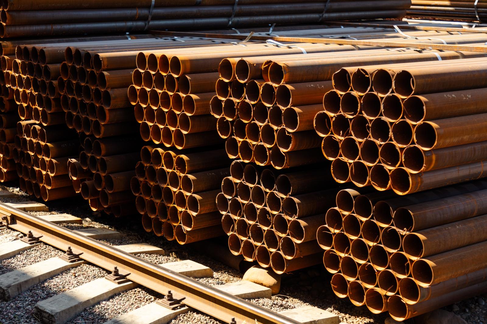 Stacks of industrial pipes stored outdoors in sunlight as project surplus or yard stock